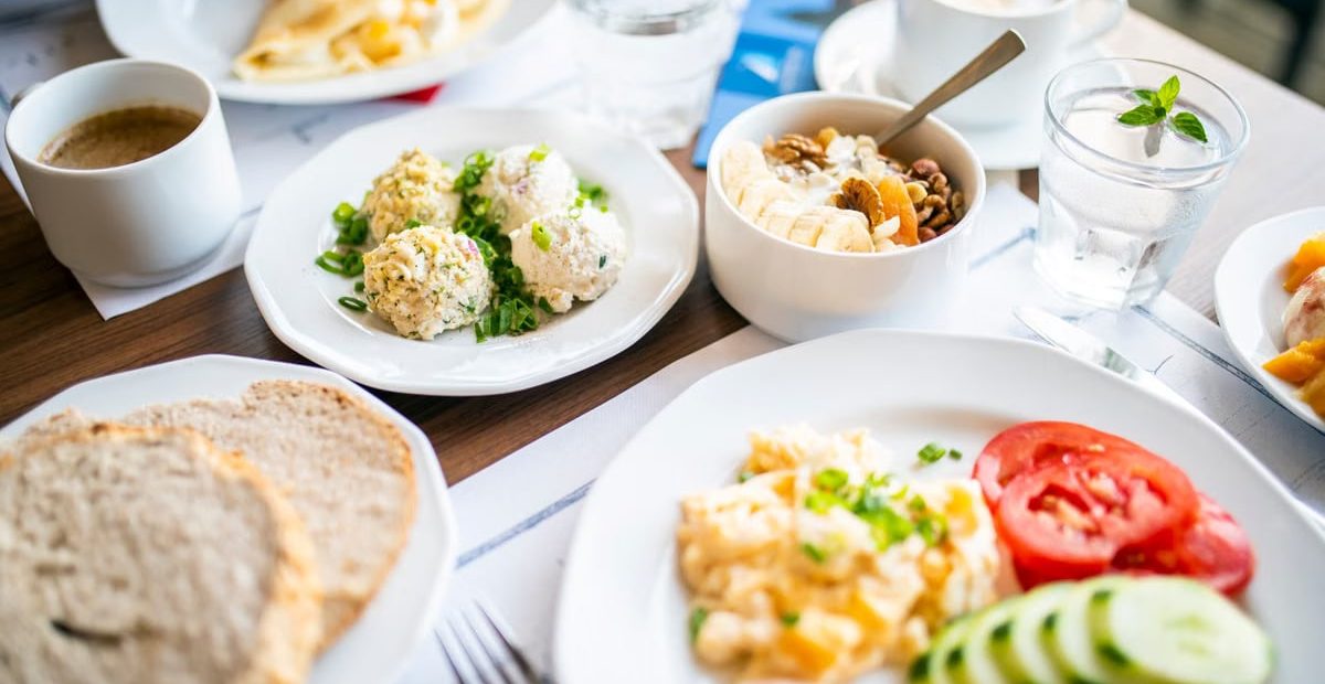 From above of tasty brunch of power bowl and scrambled eggs with fresh vegetable slices against drinks on table