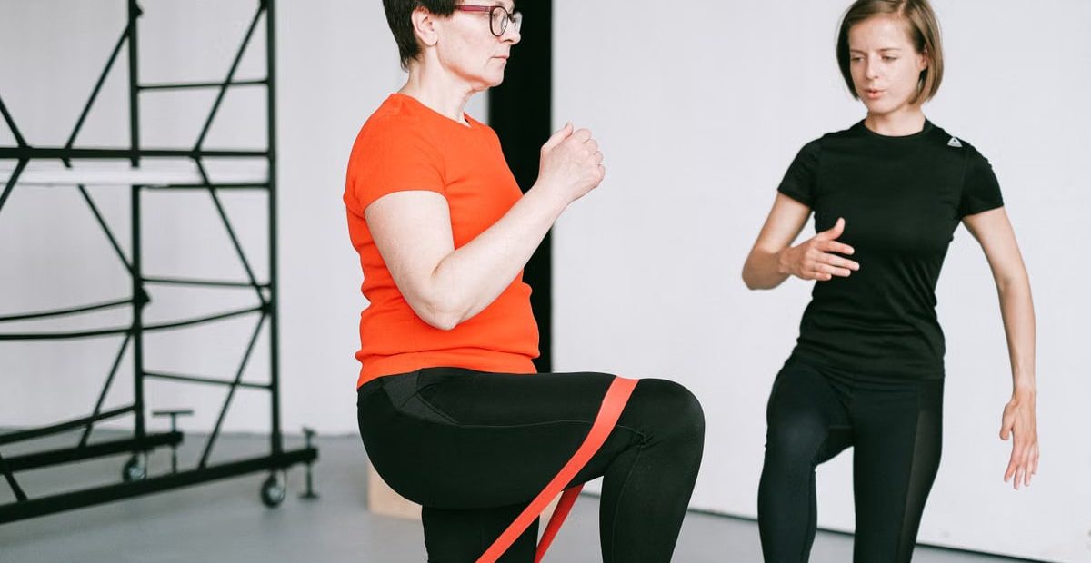 Personal trainer guiding a woman with resistance band exercise in a gym setting.