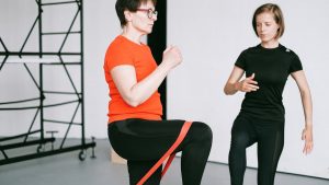 Personal trainer guiding a woman with resistance band exercise in a gym setting.