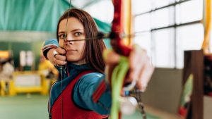 Woman archer aiming with bow indoors, emphasizing precision and focus.